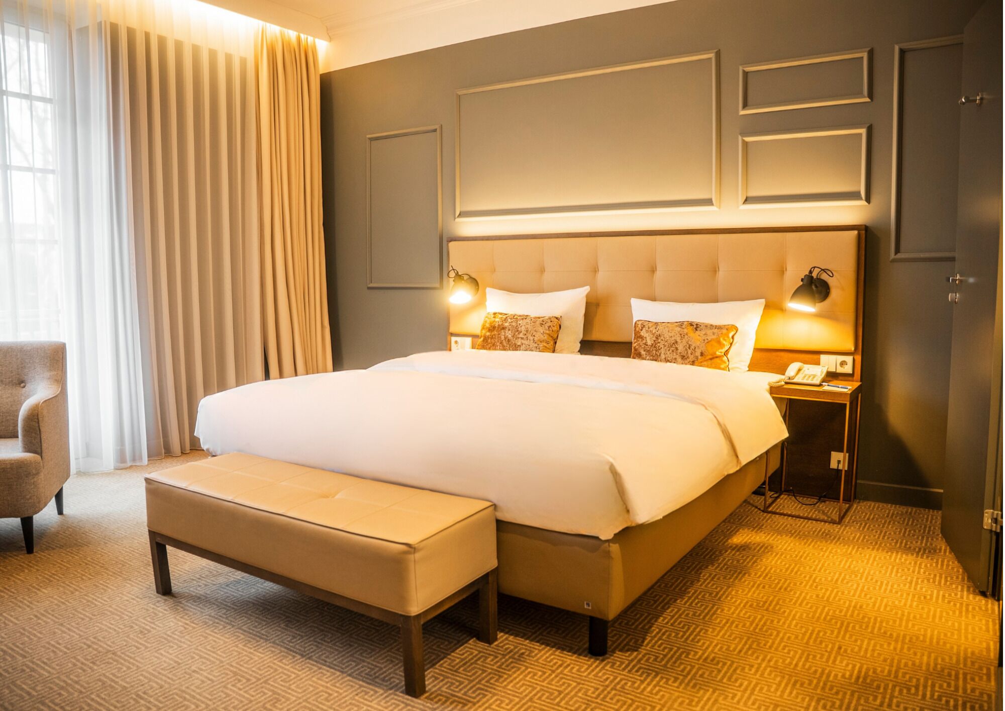 A hotel room with a large bed, bedside lamps, a chair, and a desk with a phone.