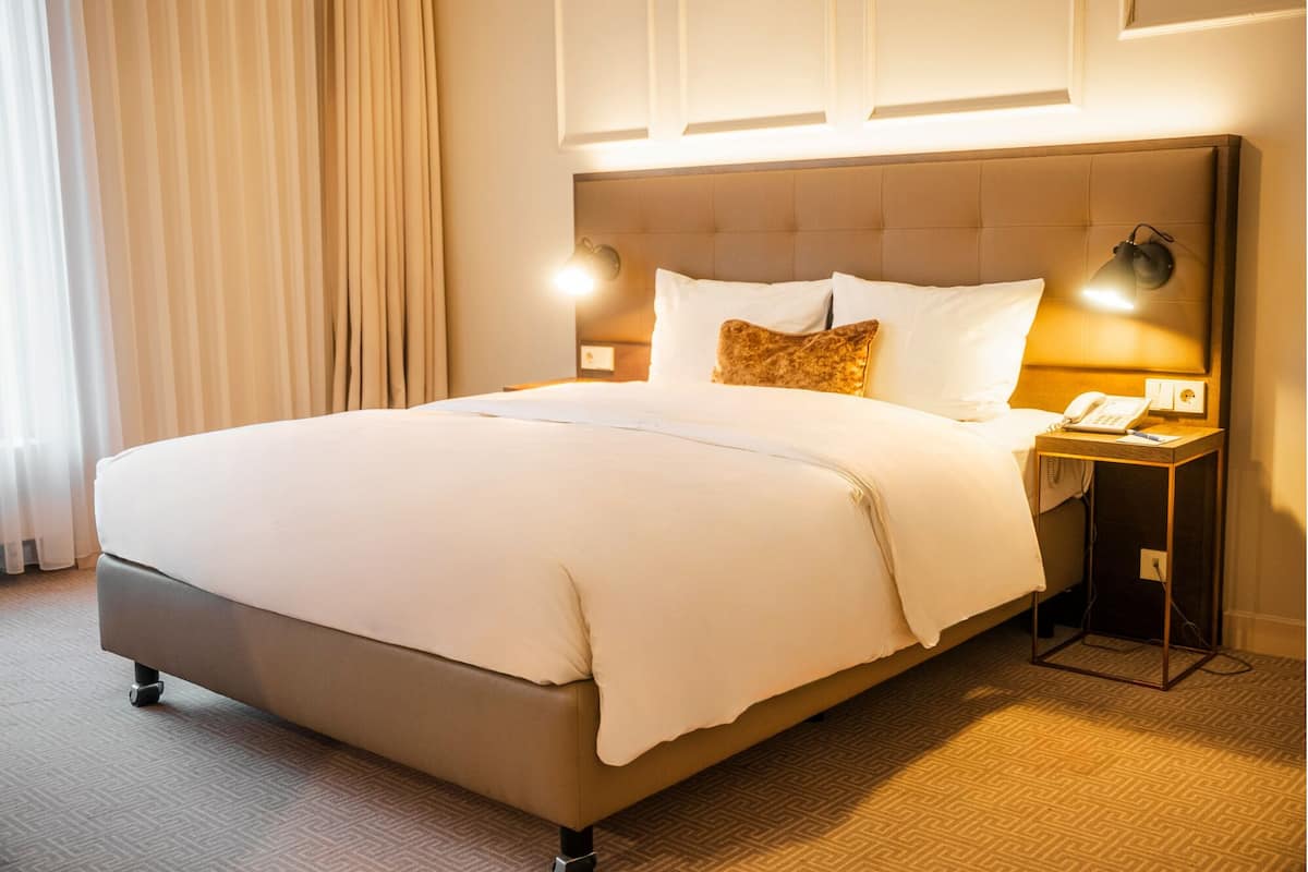 A hotel room with a large bed, a bedside table with a lamp, and a telephone.