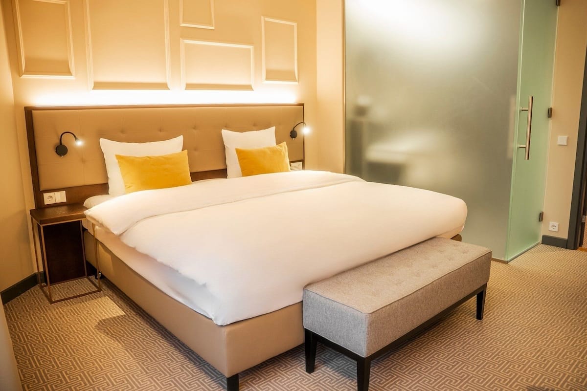 A hotel room with a large bed, a bench, a nightstand, and a wardrobe.