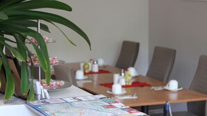 Un coin repas avec une table en bois dressée pour deux personnes, une carte et une plante à feuilles vertes.