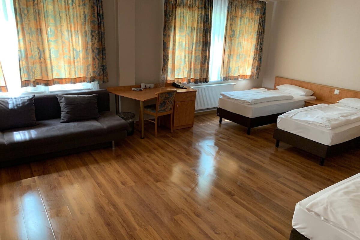 A hotel room with a wooden floor, a sofa, a desk, two single beds, and curtains.
