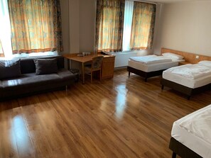 Habitación de hotel con suelo de madera, sofá, escritorio, dos camas individuales y cortinas.