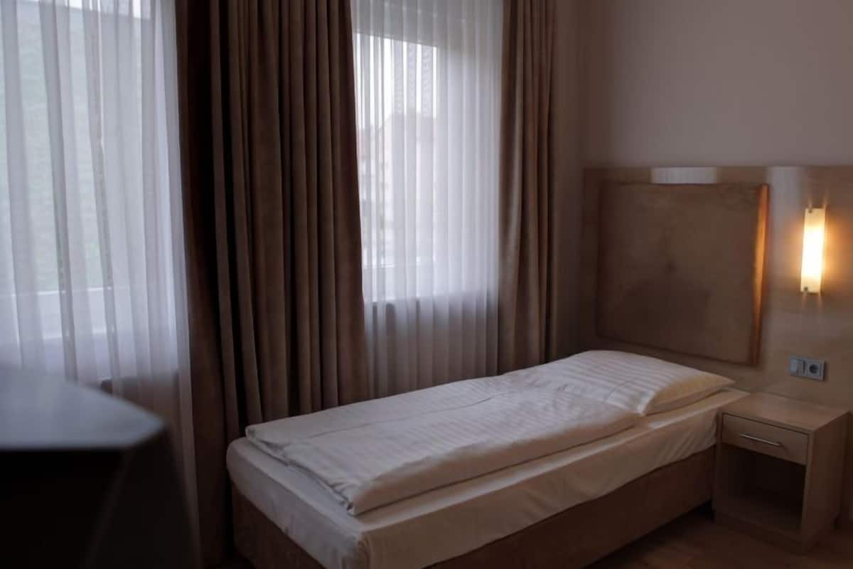 A single bed with a headboard, a bedside table, and a wall-mounted light.