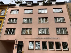 A multi-story hotel with a pink facade, multiple windows, and a sign indicating "Hotel Am Kurfürstenplatz".