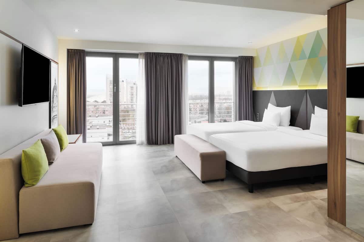Ein modernes Hotelzimmer mit einem großen Bett, einer Couch, einem Fernseher und Blick auf die Stadt.