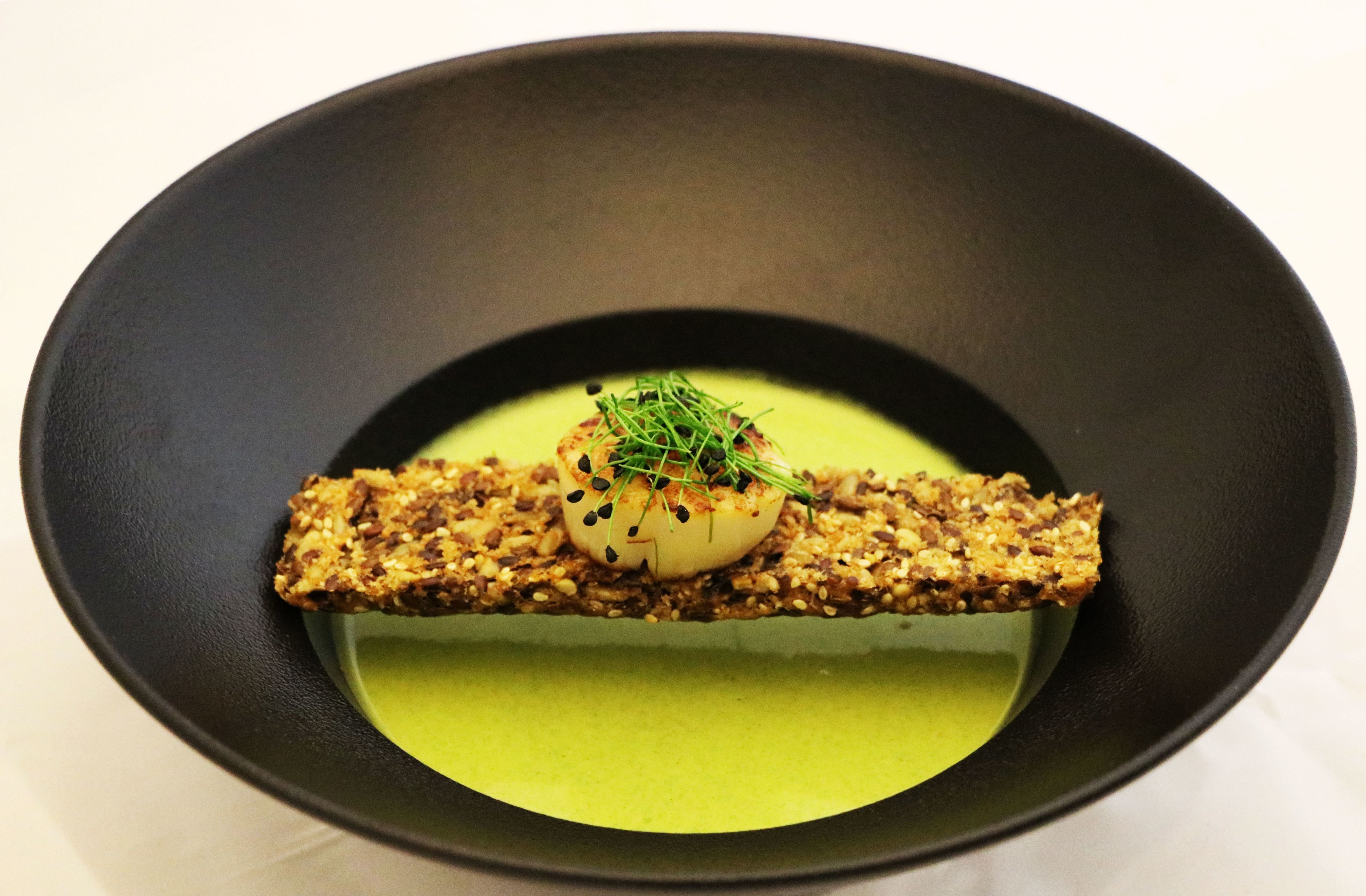 A dish with a green sauce base, a seared item, and a garnish on top.