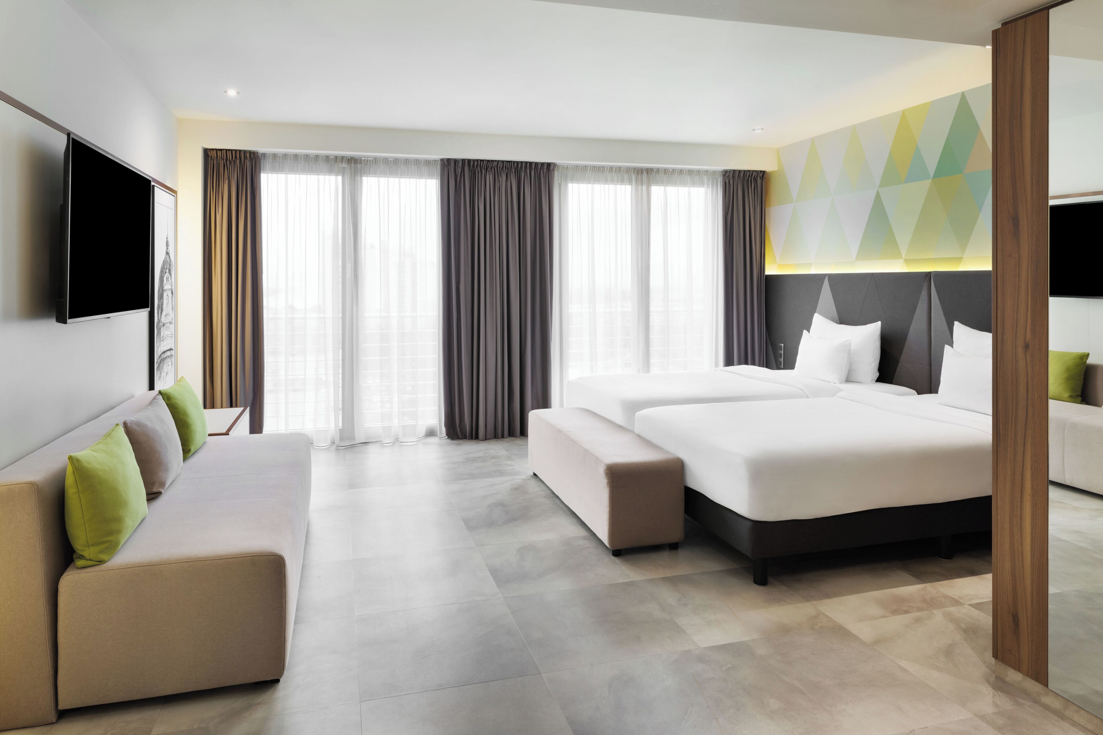 Een moderne hotelkamer met een bank, een bed, een televisie en een groot raam met gordijnen.