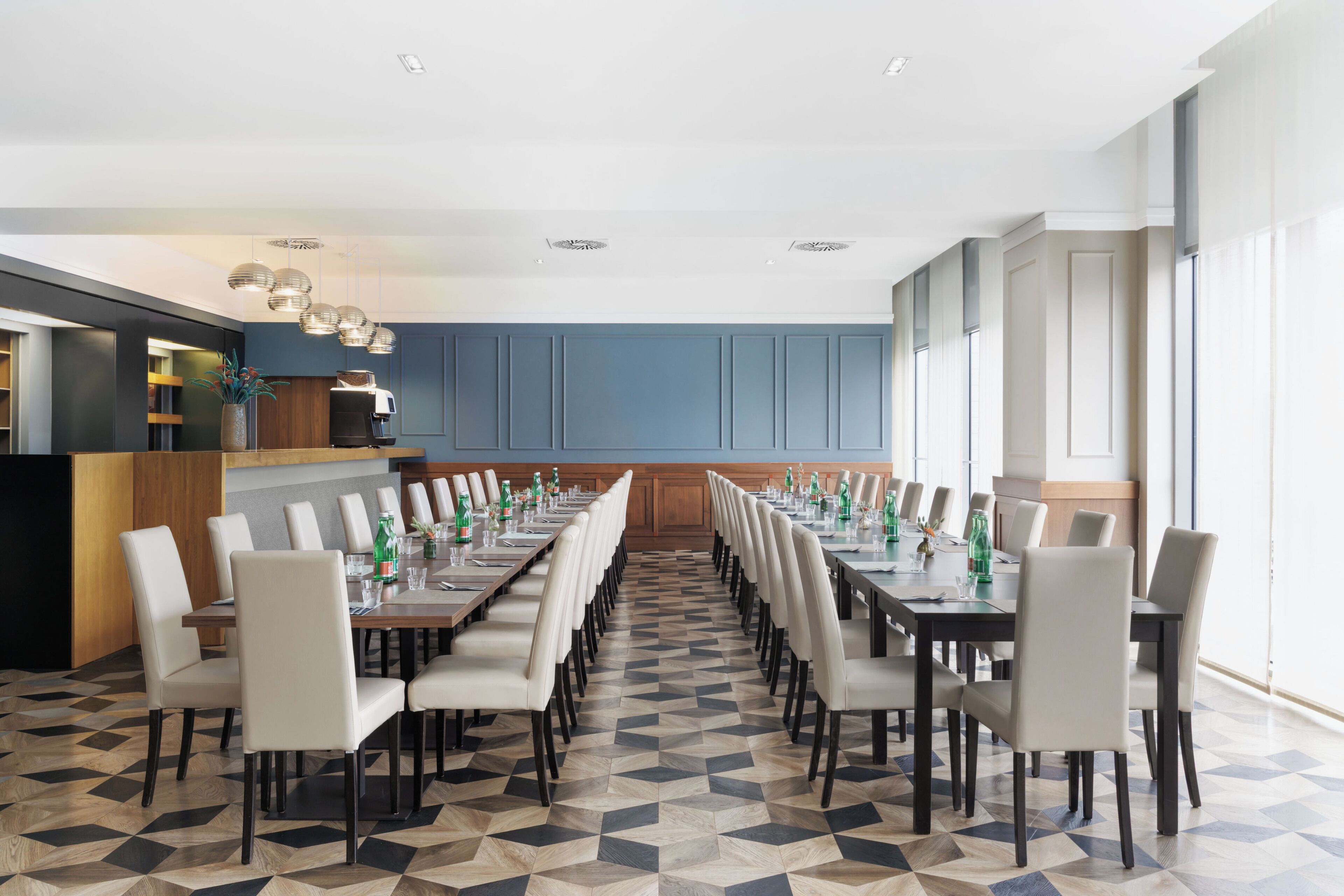 Un salón de conferencias con una larga mesa, sillas y una cocina al fondo.
