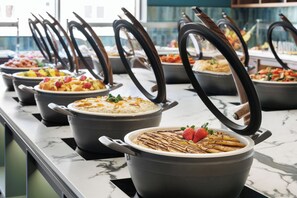 Een buffet met diverse gerechten in potten, waarvan sommige deksels open hebben.