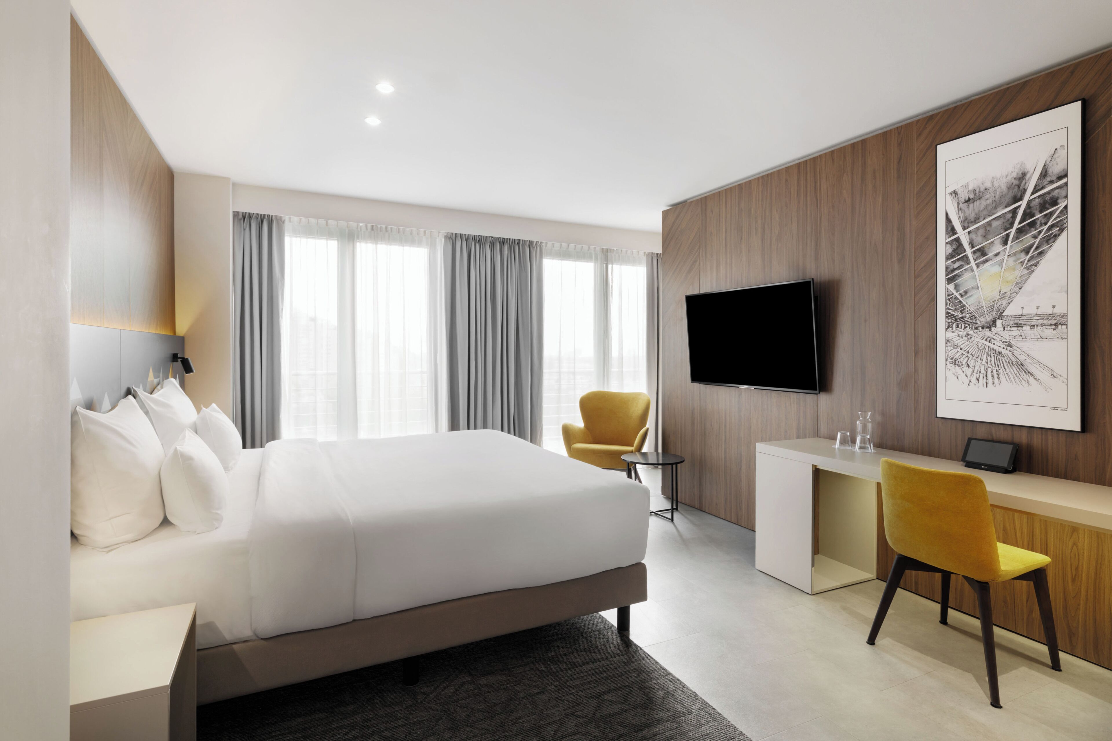 A modern hotel room with a large bed, a desk, a chair, a flat-screen TV, and a large window with curtains.