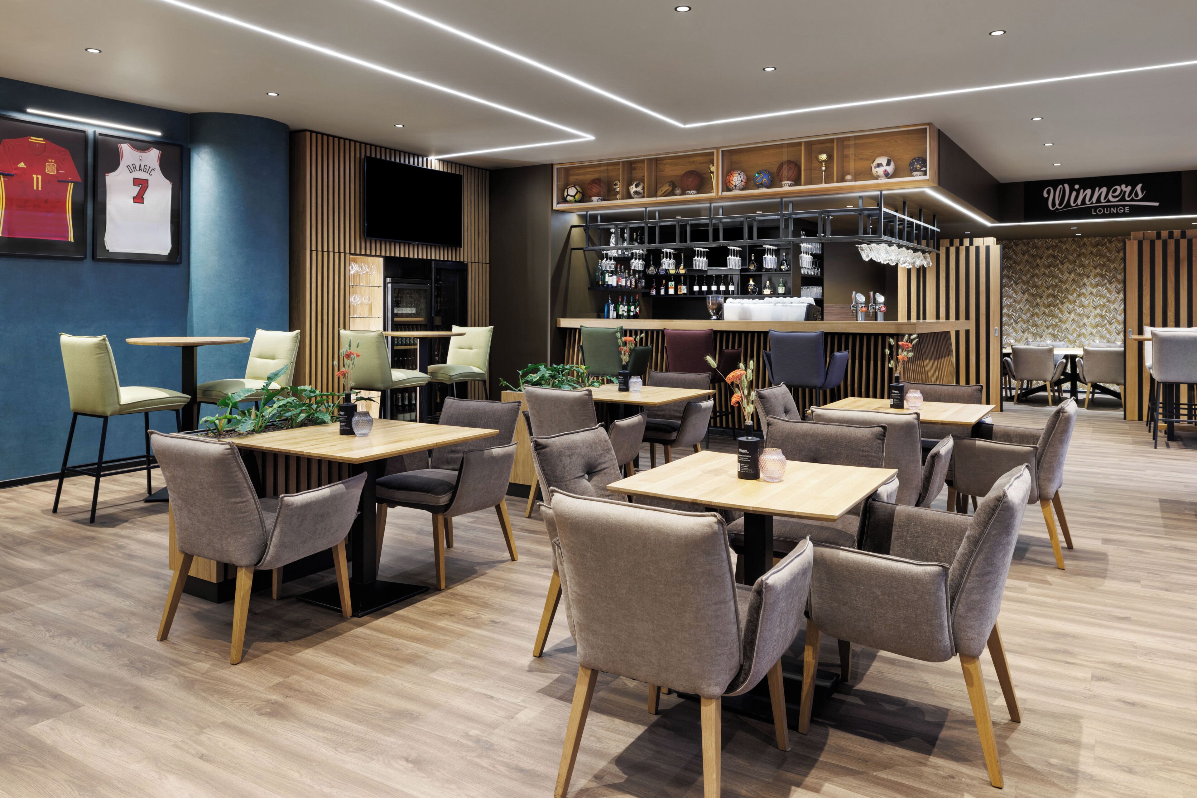 A modern lounge area with multiple seating arrangements, a bar with shelves of bottles, and a television mounted on the wall.