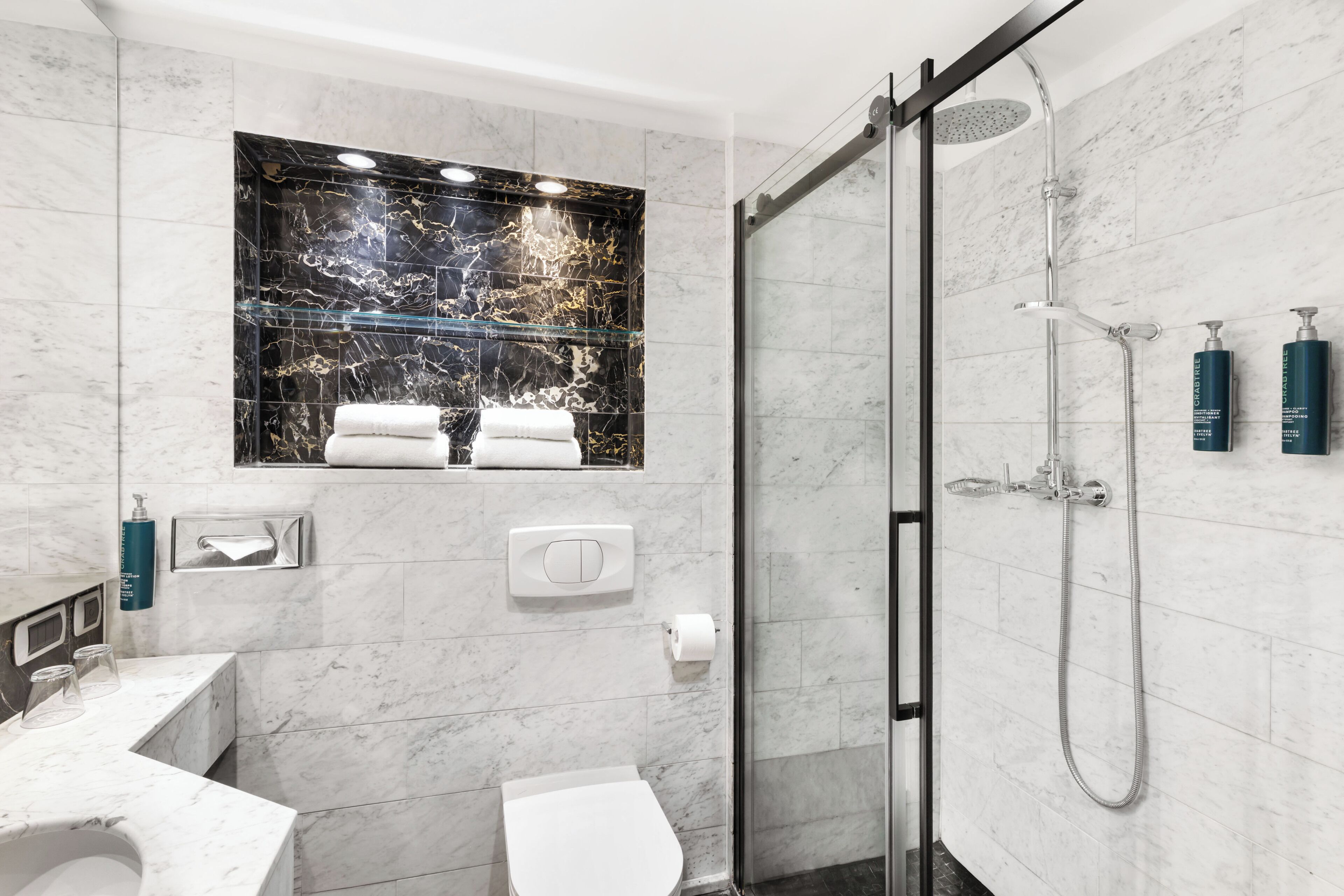 Een moderne badkamer met een glazen douchecabine, een marmeren wastafelmeubel en een toilet.