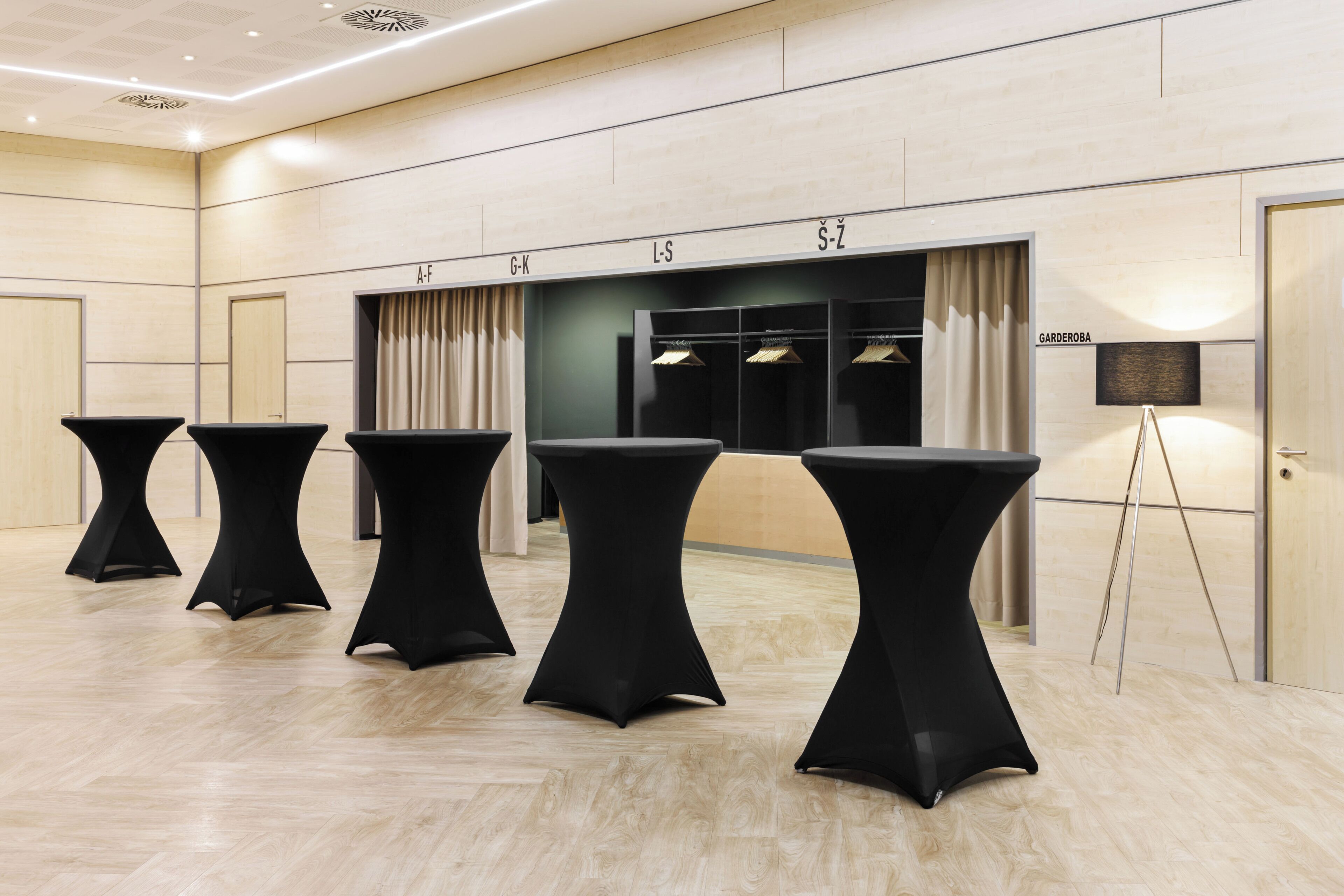 A hotel room with a wooden floor, black tables, a mirror, and a sign with room numbers.