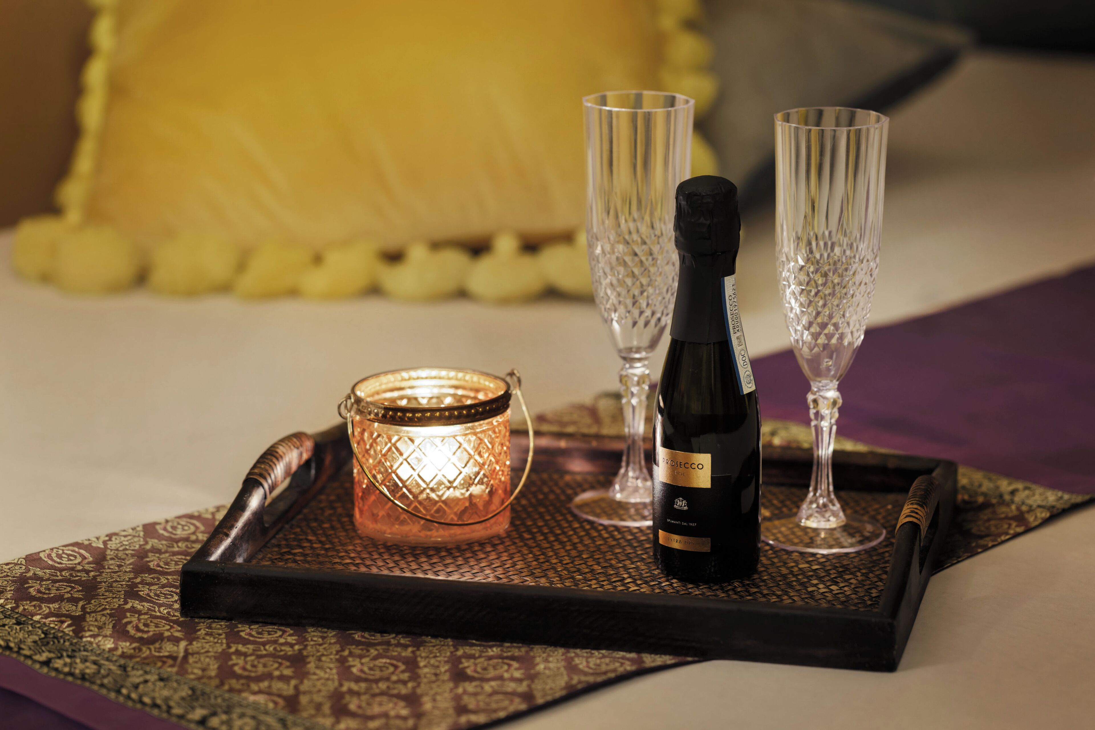 A tray with a bottle of wine, two glasses, and a candle on a patterned tablecloth.