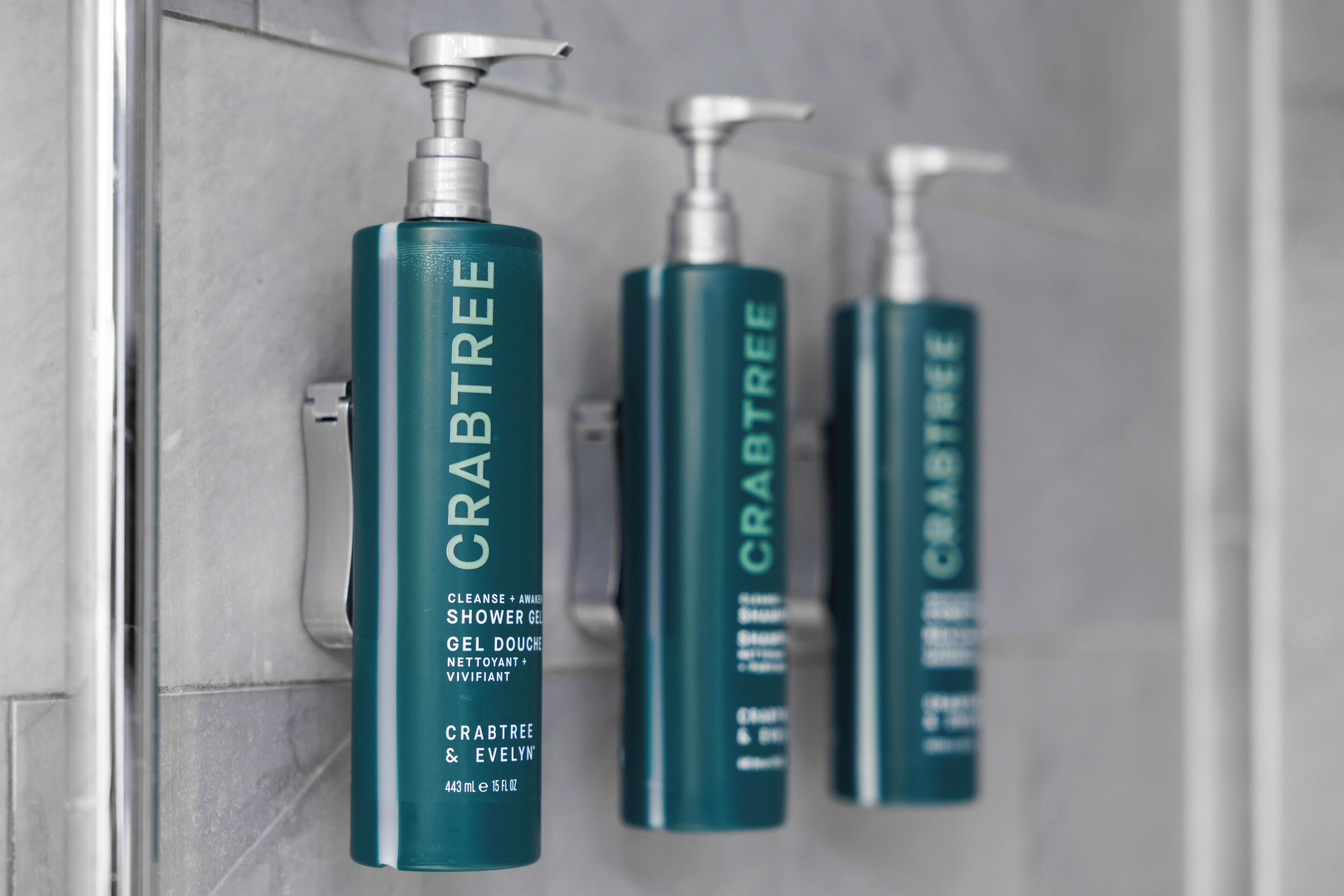 Three bottles of Crabtree shower gel hanging on a tiled wall.