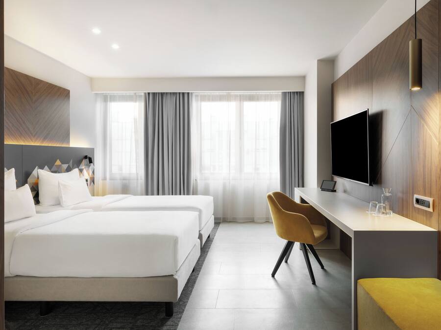 Une chambre d’hôtel avec deux lits, un bureau, une chaise, une télévision et une fenêtre avec des rideaux.