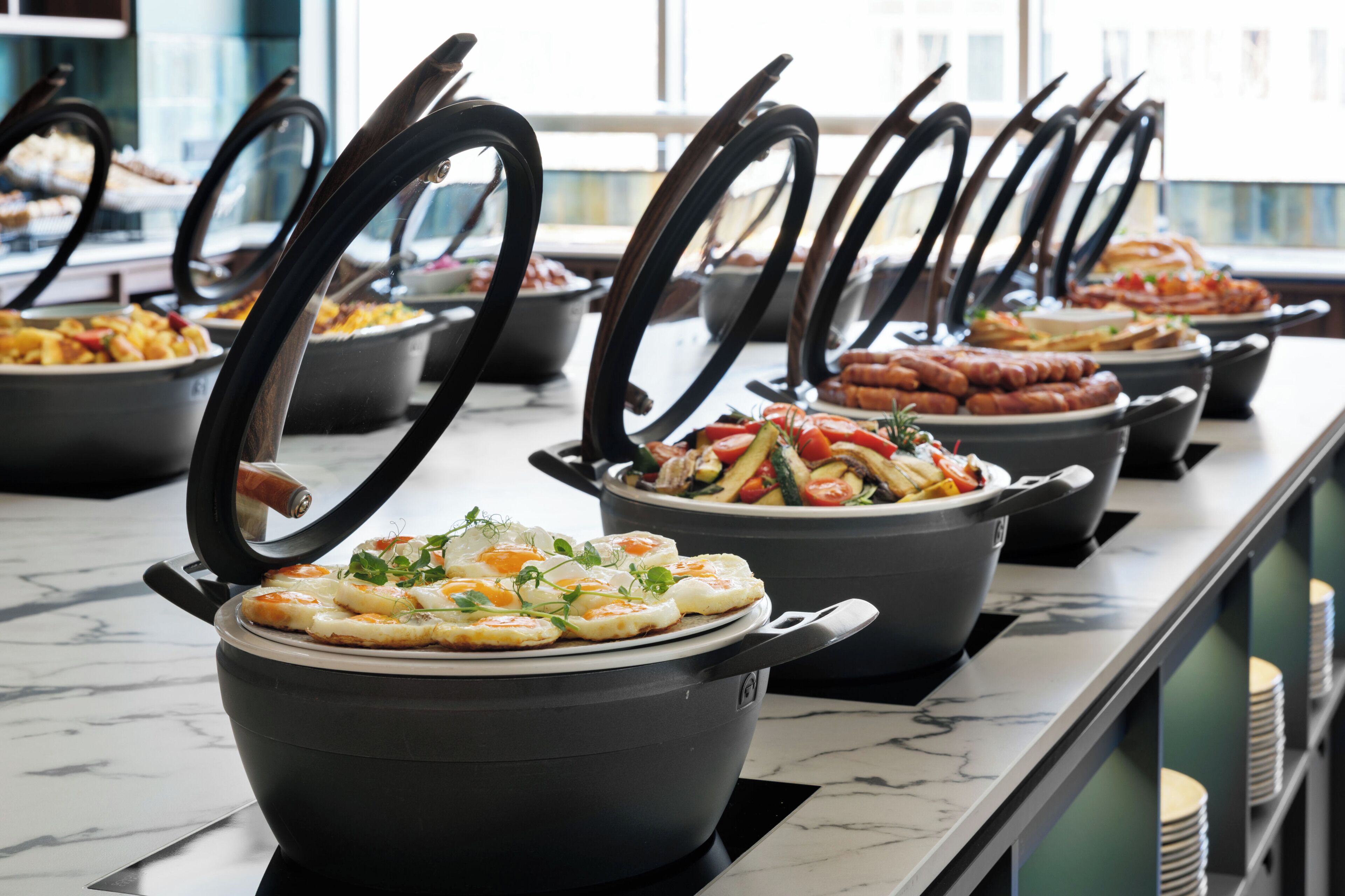 Een buffet met diverse gerechten in grote potten en kommen, gerangschikt op een marmeren aanrecht.