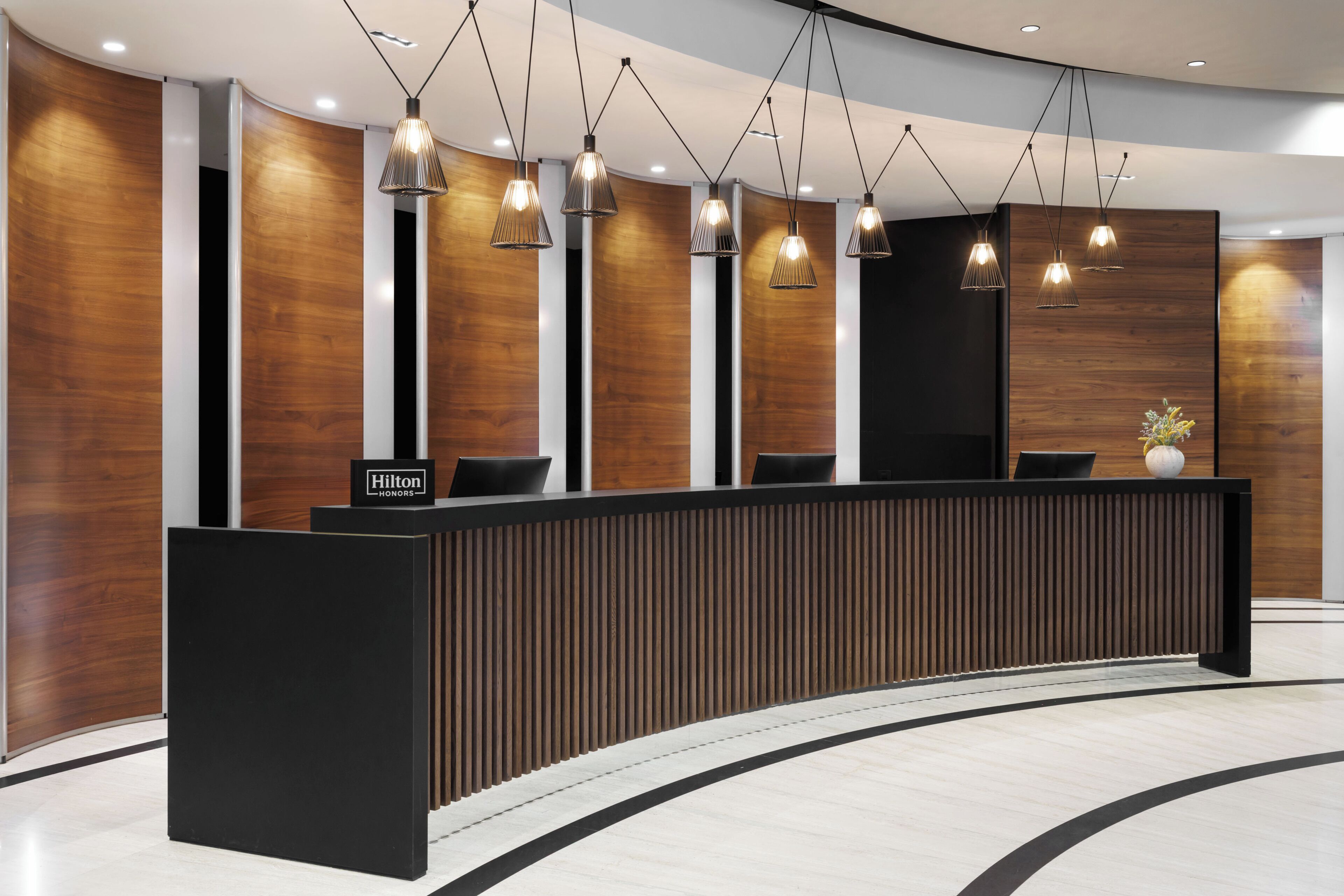 A modern hotel reception desk with a curved design, multiple pendant lights, and a 'Hilton Honors' sign.