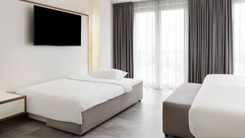 A modern hotel room with a bed, a bedside table, a flat-screen TV mounted on the wall, and a large window with curtains.