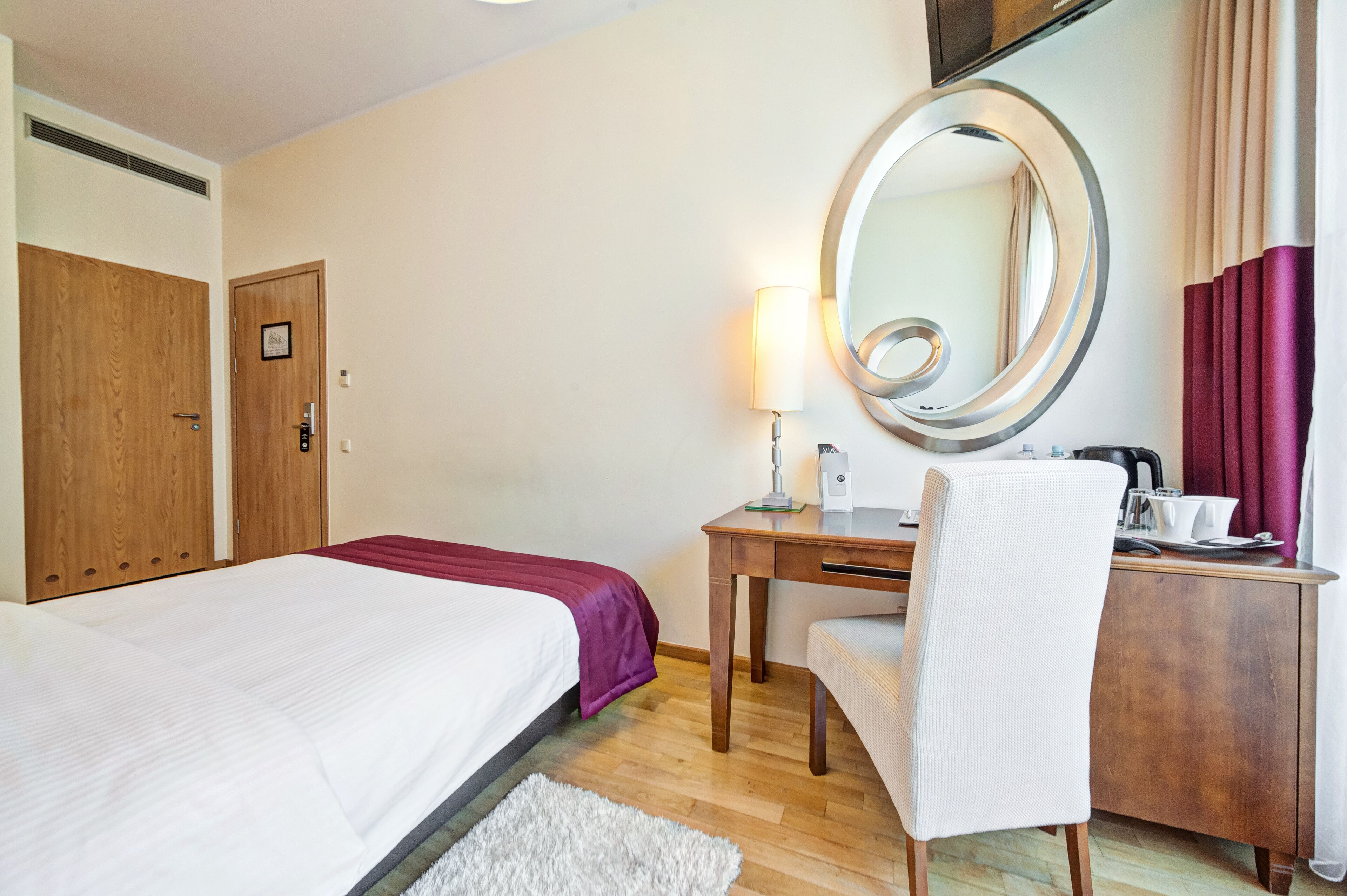 Ein Hotelzimmer mit Bett, Schreibtisch, Stuhl, Spiegel, Lampe und Kleiderschrank.