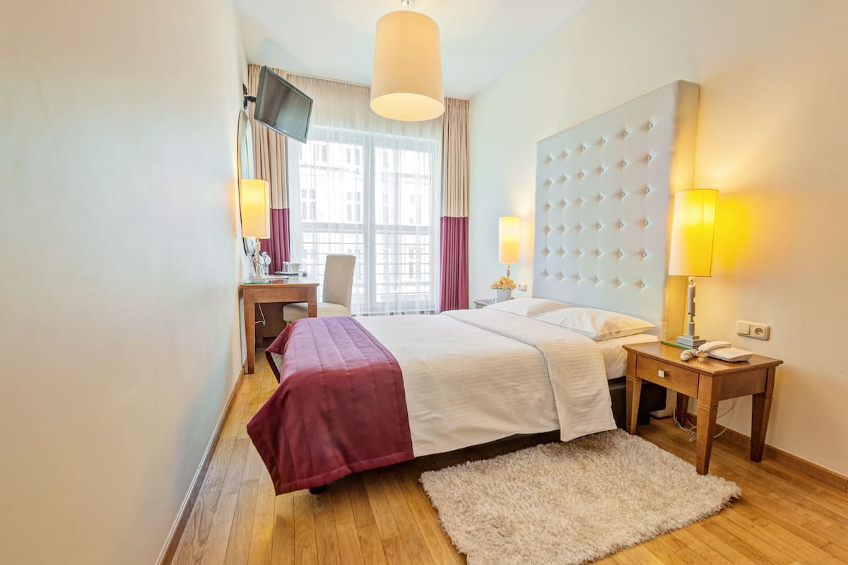 A hotel room with a large bed, a desk, a chair, a TV, and a window with curtains.