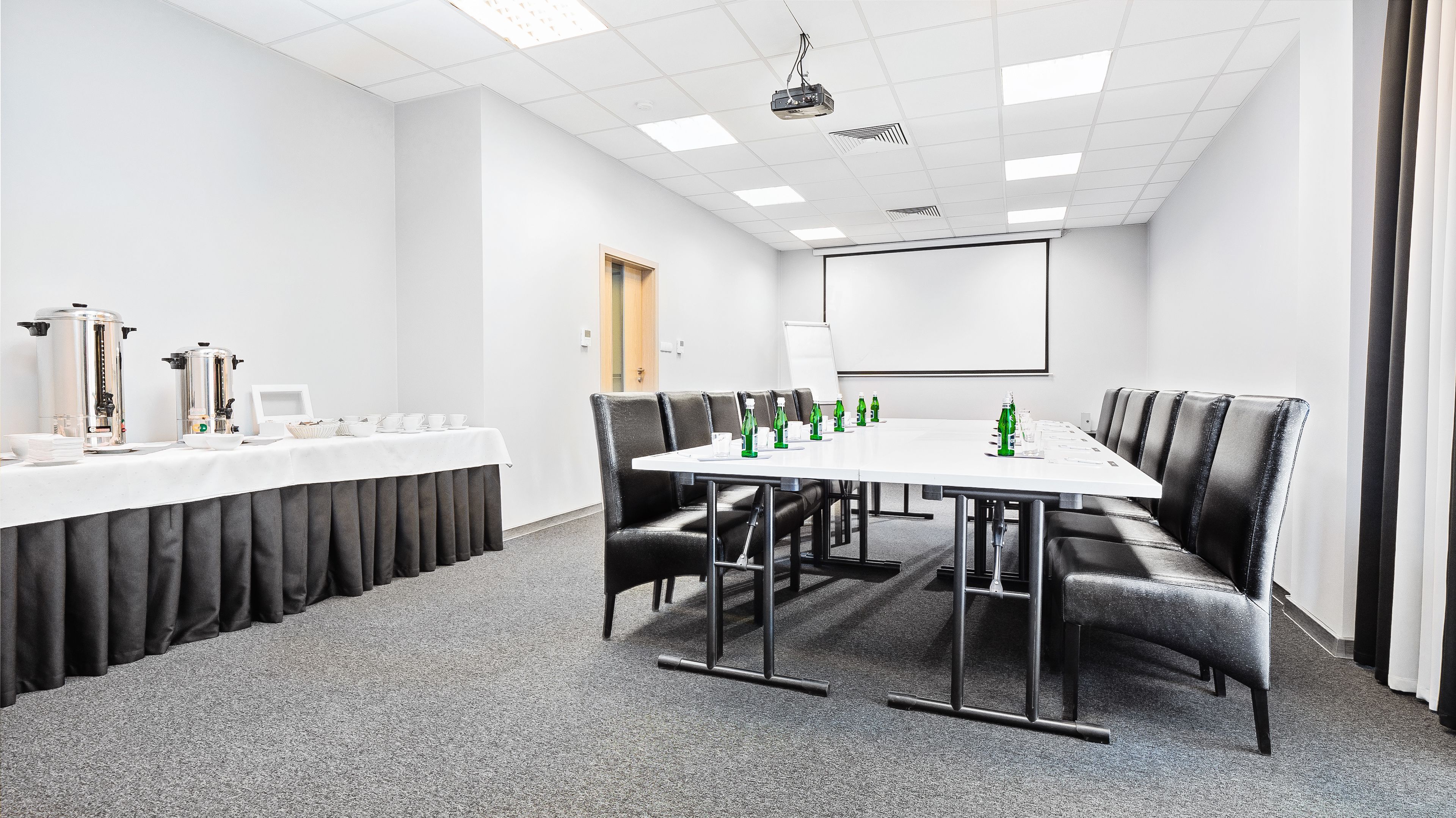 A conference room with a long table, black leather chairs, a white tablecloth, and a projector screen.