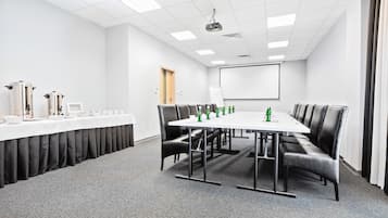 Une salle de conférence avec une longue table, des fauteuils en cuir noir, une nappe blanche et un écran de projection.