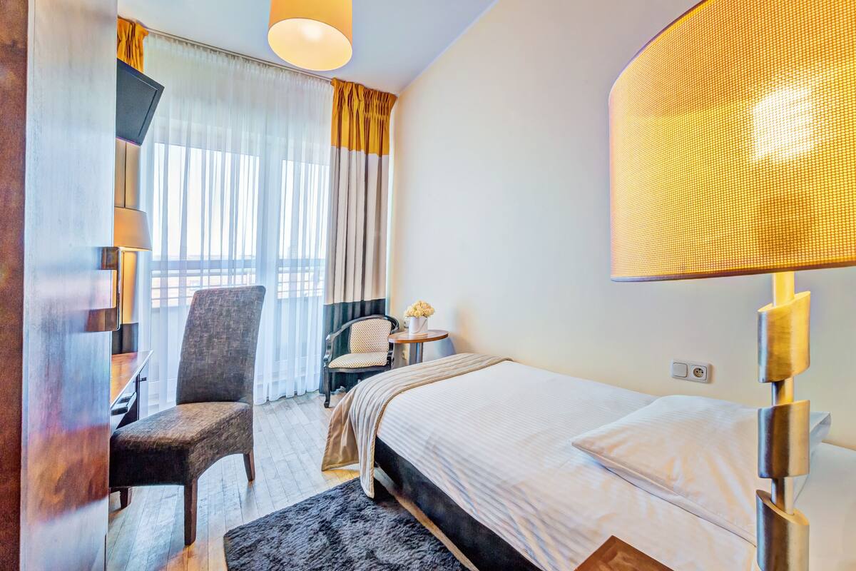 A hotel room with a bed, a chair, a desk, and a lamp.