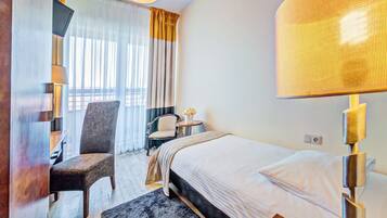 A hotel room with a bed, a chair, a desk, and a lamp.