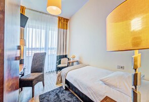 A hotel room with a bed, a chair, a desk, and a lamp.