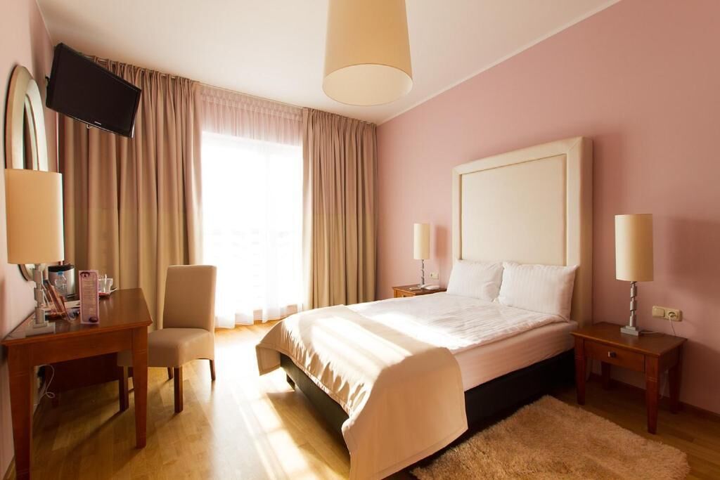 Habitación de hotel con cama, dos mesitas de noche, una silla, televisión y ventana con cortinas.