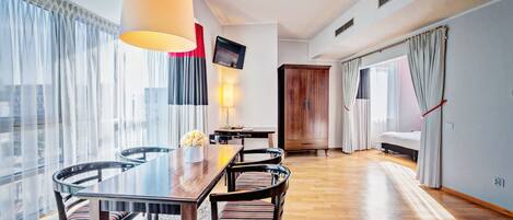 Une chambre d’hôtel moderne équipée d’un coin repas, d’une télévision, d’une armoire et d’un lit.