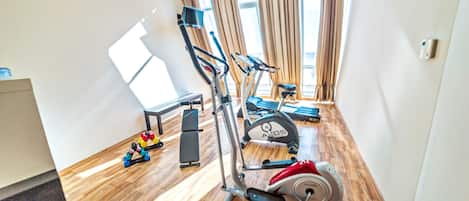 A spacious room with wooden flooring, a treadmill, an elliptical, and a bench.