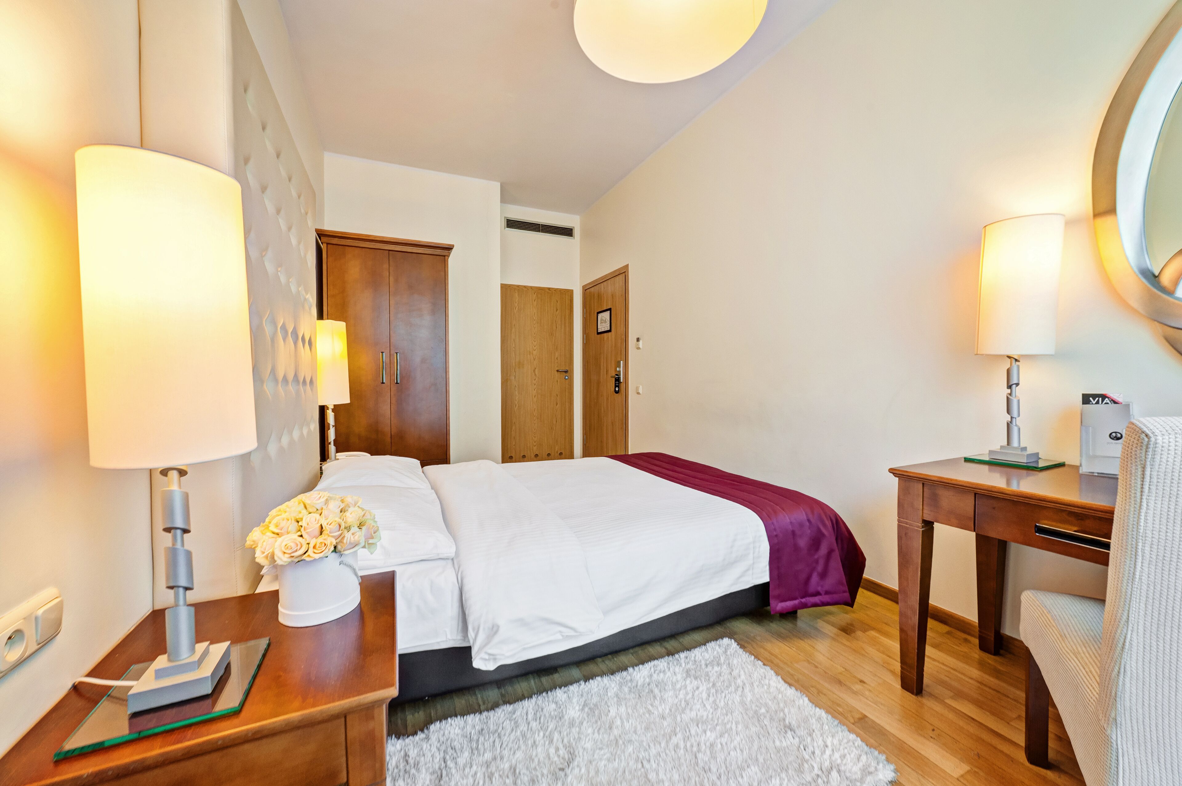 Habitación de hotel ordenada con cama, mesitas de noche, escritorio y espejo.
