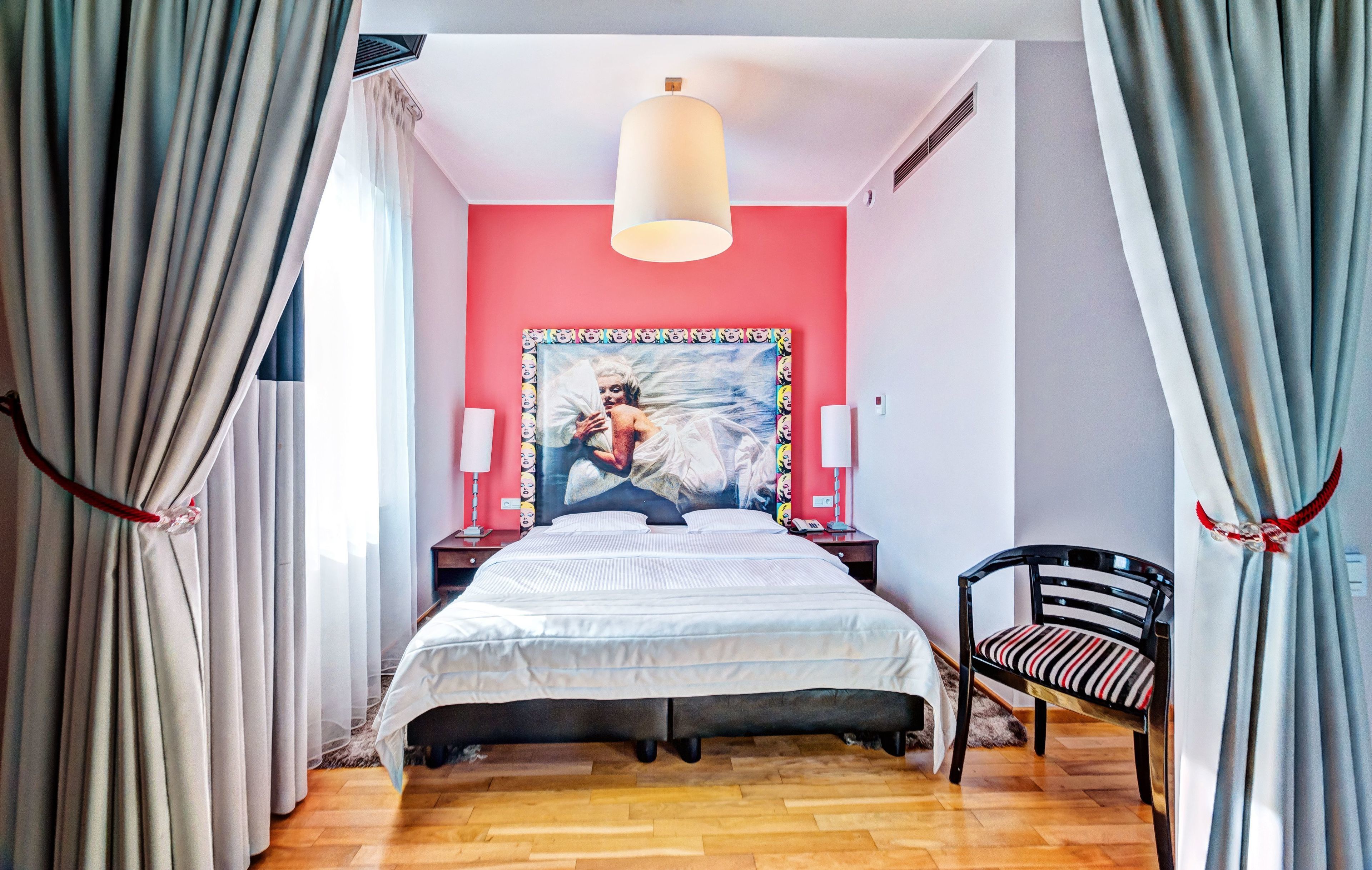 Quarto com cama, uma cadeira, um quadro e uma luminária.