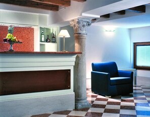 A reception area with a marble counter, a blue chair, and a checkered floor. - Hotel Giudecca Venezia (Venice)