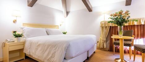 A hotel room with a bed, bedside table, lamp, chair, and a small table with a vase.