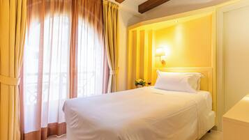A hotel room with a bed, curtains, a wall-mounted lamp, and a flower vase.
