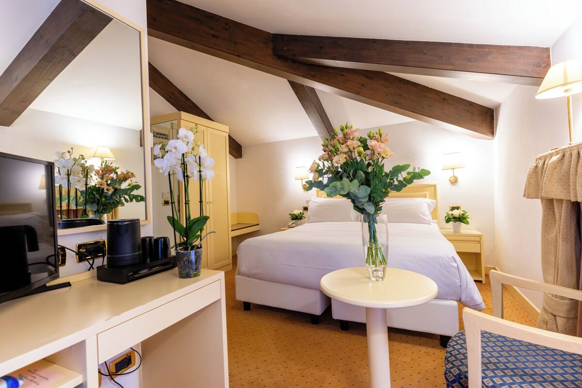 A hotel room with a bed, bedside table, lamp, mirror, desk with a computer, and a TV.