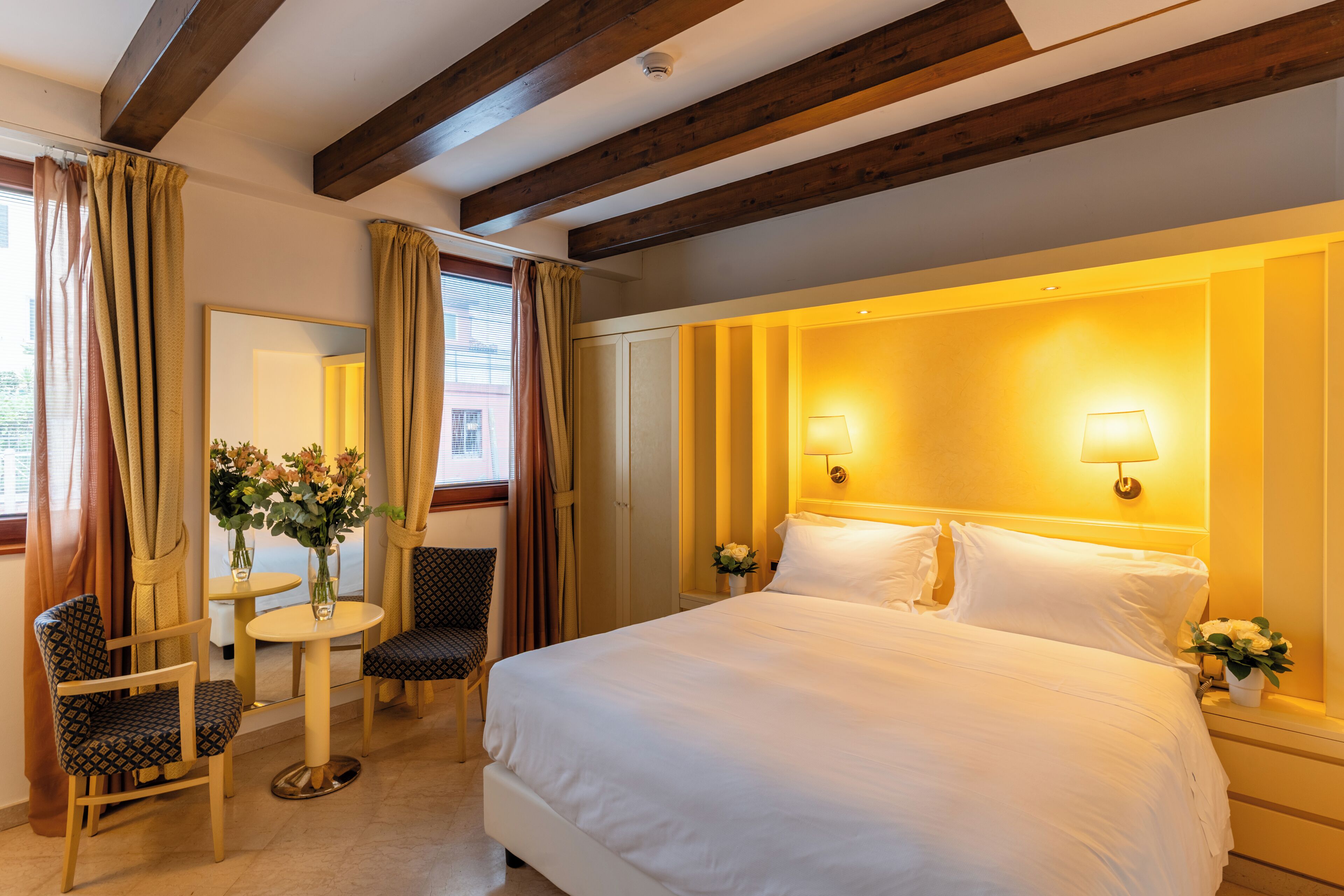 Une chambre d’hôtel avec un grand lit, deux lampes de chevet, une petite table ronde avec des chaises et un miroir.