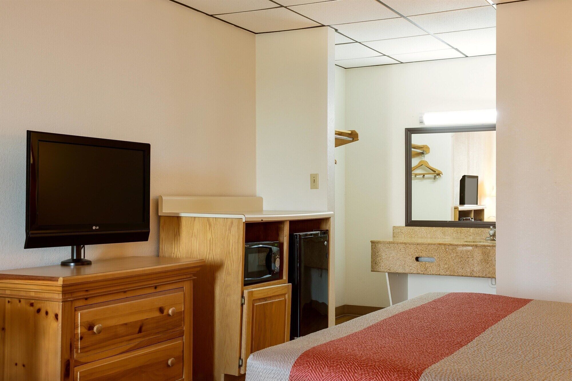 Habitació d'hotel amb televisió, un taulell de fusta, microones i un llit amb manta a ratlles.