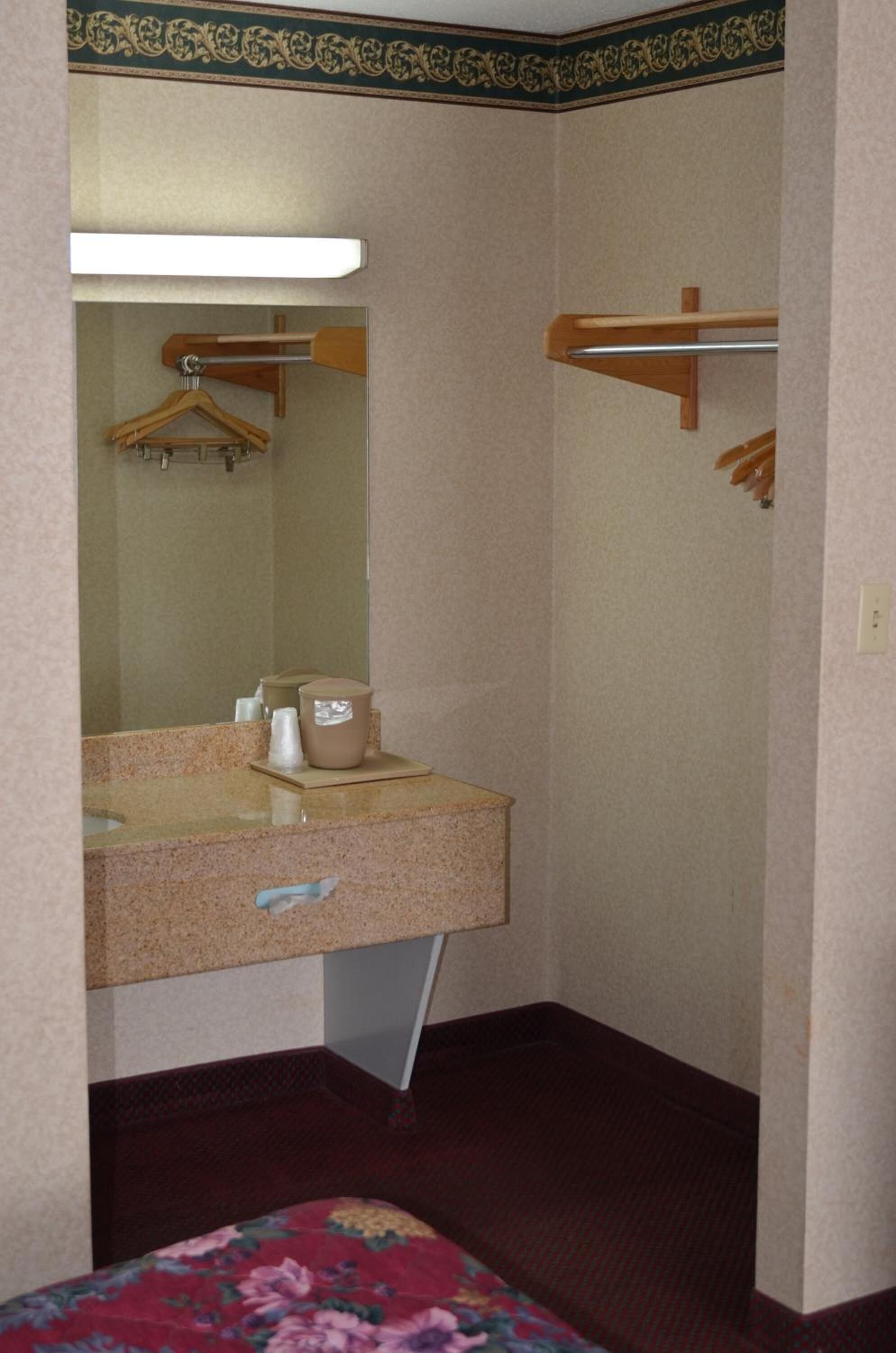 Un baño de hotel pequeño con lavamanos, espejo, toallero y cama con colcha estampada.
