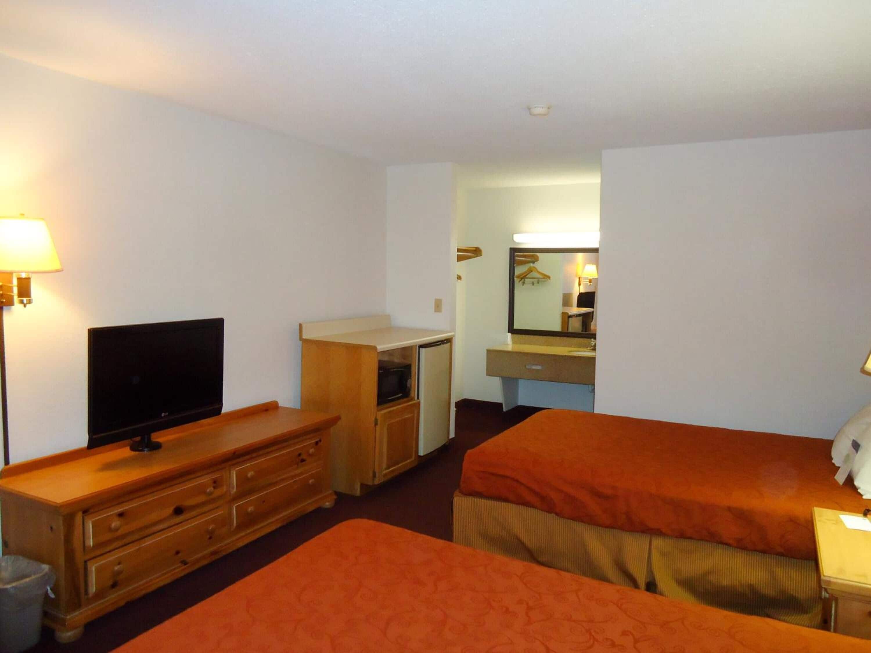 A hotel room with two beds, a TV, a dresser, a desk with a mirror, and a lamp.