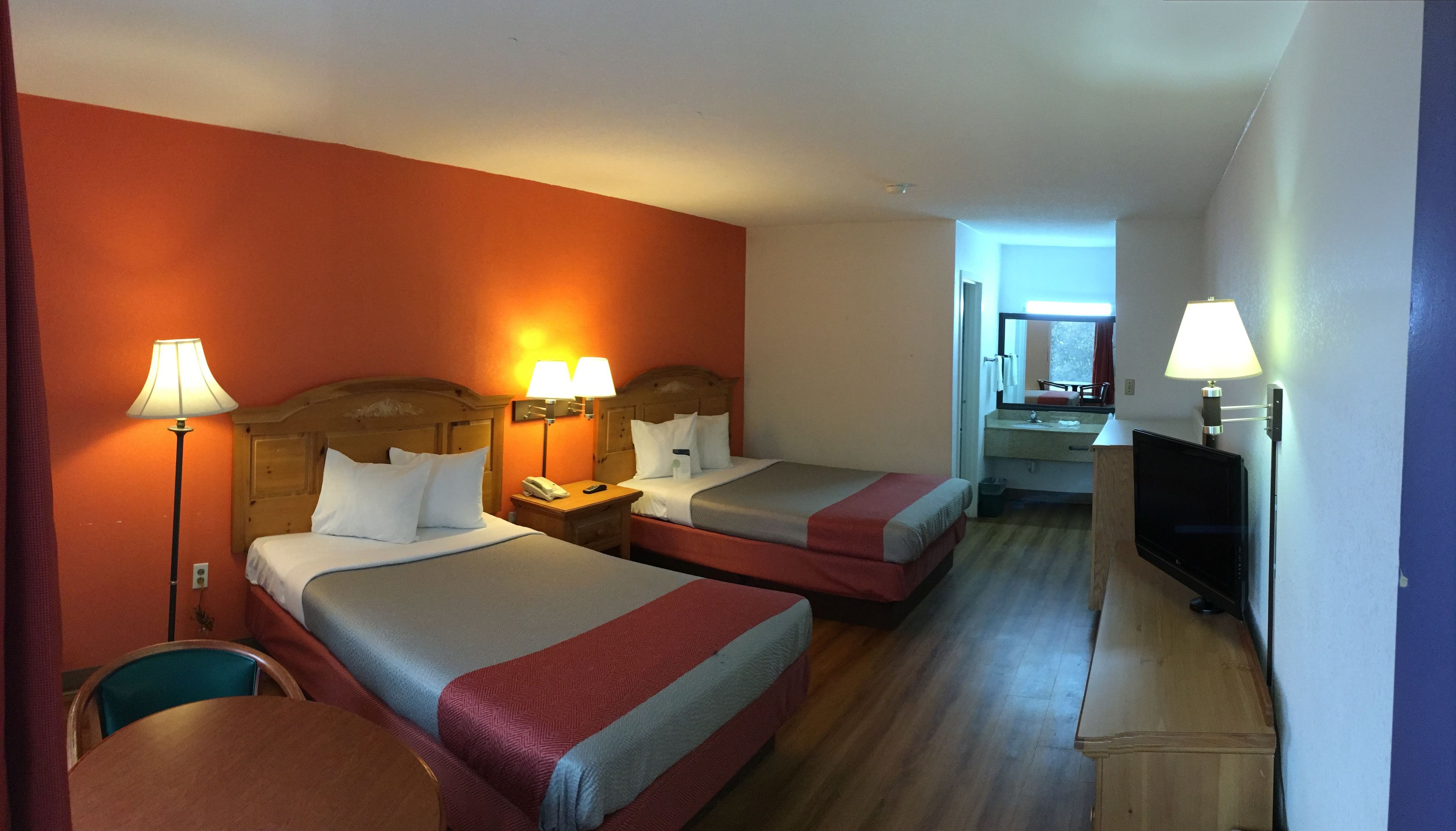A hotel room with two beds, a desk, a chair, a TV, and a bathroom visible in the background.