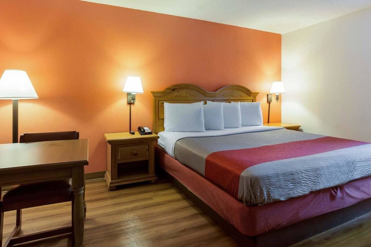 Una habitación de hotel con una cama, dos mesitas de noche con lámparas, una silla de madera y un escritorio.