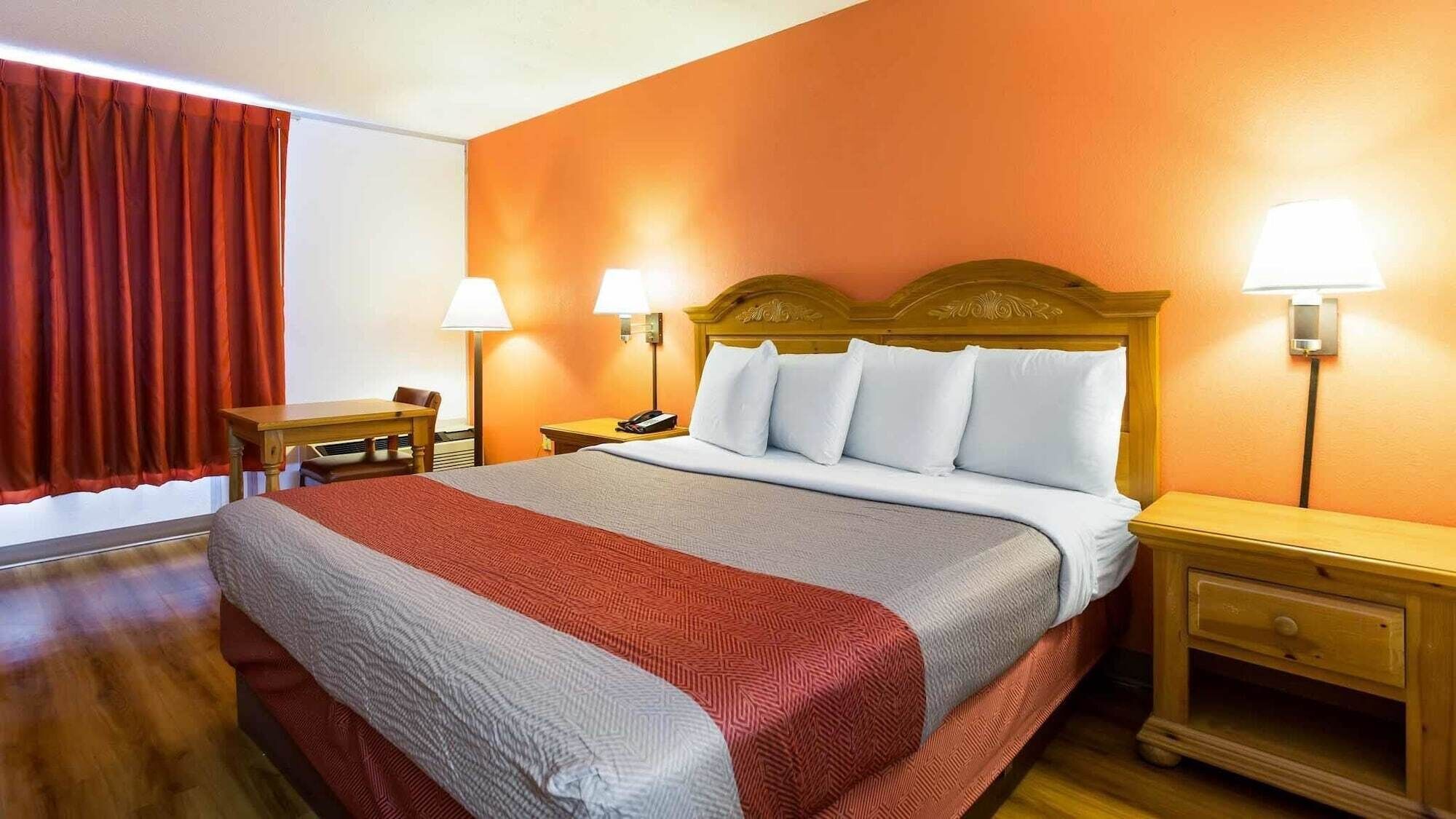 Una habitación de hotel con una cama, dos mesitas de noche, un escritorio, una silla y dos lámparas.