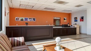 Un vestíbulo de hotel con una pared naranja, un mostrador de recepción, un sofá, una mesa de centro y una planta en maceta.