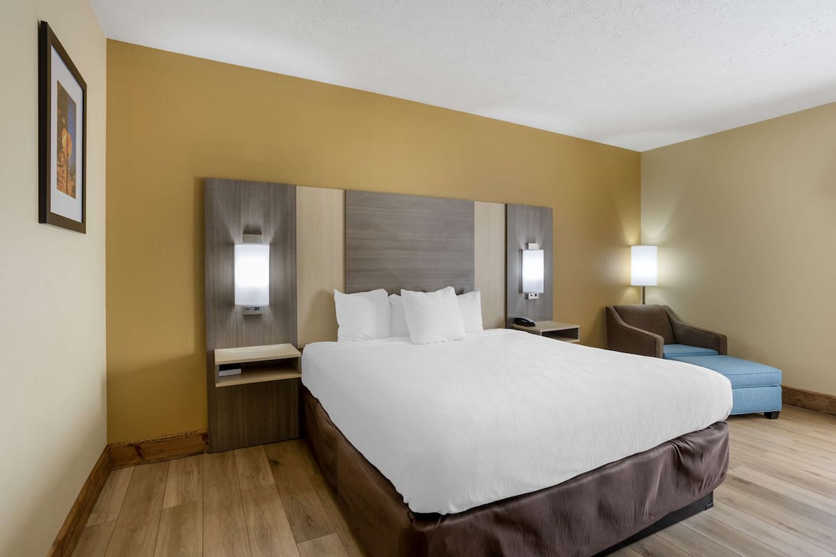 A hotel room with a large bed, bedside tables, a desk, a chair, and a lamp.