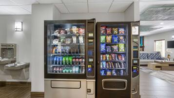 A hotel lobby with two self-service beverage vending machines stocked with various drinks and snacks.