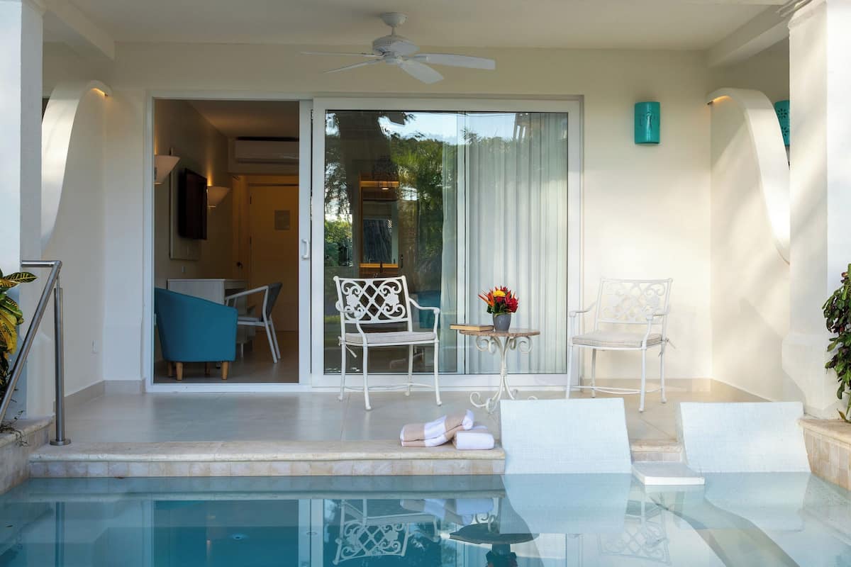 Un espace piscine agrémenté d’une table en verre, de deux chaises blanches et d’une petite table sur laquelle est posé un vase de fleurs.